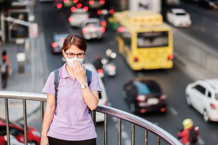 young Asian woman wearing N95 respiratory mask protect and filter pm2.5 (particulate matter) against traffic and dust city. healthcare and air pollution conceptの写真素材