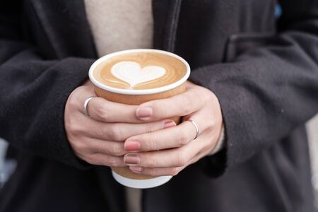 Woman hands holding Hot coffee paper cup, heart shape latte coffee art. Love, holiday, Valentine day and free plastic container conceptの写真素材