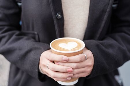 Woman hands holding Hot coffee paper cup, heart shape latte coffee art. Love, holiday, Valentine day and free plastic container conceptの写真素材