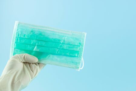 Hand with medical glove holding Protective face mask on blue background.