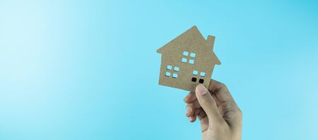 hand holding house model on blue background with copy space for text. Banking, real estate, investment, financial, savings conceptsの写真素材