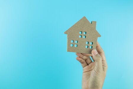 hand holding house model on blue background with copy space for text. Banking, real estate, investment, financial, savings conceptsの写真素材