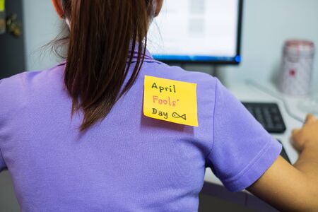 Back of young woman office with a white paper note attached with the text happy april fools dayの写真素材
