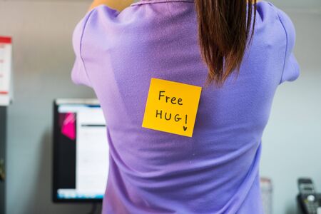 Back of young woman office with a yellow sticky note attached with the text Free Hug. happy april fools day conceptの写真素材
