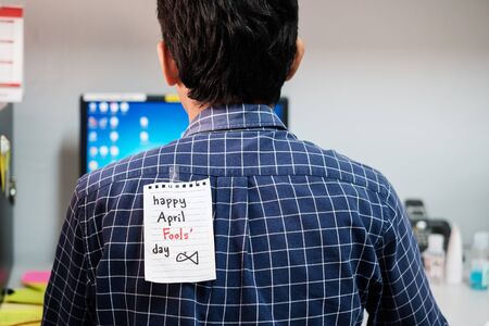 Back of young man office with a white paper note attached with the text happy april fools dayの写真素材