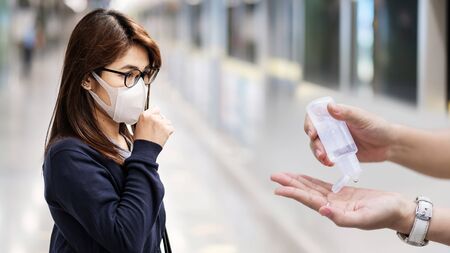 young Asian woman wearing surgical face mask versus hand using wash hand sanitizer gel dispenser against Novel coronavirus or Corona Virus Disease (Covid-19) at airport. Hygiene and Healthcare conceptの写真素材