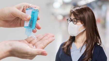 young Asian woman wearing surgical face mask versus hand using wash hand sanitizer gel dispenser against Novel coronavirus or Corona Virus Disease (Covid-19) at airport. Hygiene and Healthcare conceptの写真素材
