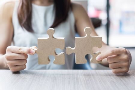 woman hands connecting couple puzzle over table, businesswoman holding wood jigsaw inside office. Business solutions, mission, target, success, goals and strategy conceptsの写真素材
