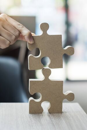 man hands connecting couple puzzle over table, businessman holding wood jigsaw inside office. Business solutions, mission, target, success, goals and strategy conceptsの写真素材