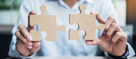 man hands connecting couple puzzle over table, businessman holding wood jigsaw inside office. Business solutions, mission, target, success, goals and strategy conceptsの写真素材