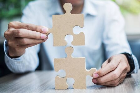 man hands connecting couple puzzle over table, businessman holding wood jigsaw inside office. Business solutions, mission, target, success, goals and strategy conceptsの写真素材