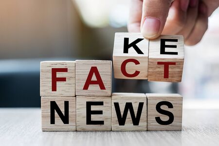 Businessman hand holding wooden cube with flip block FAKE to FACT News word on table background. News, solution and business  conceptsの写真素材