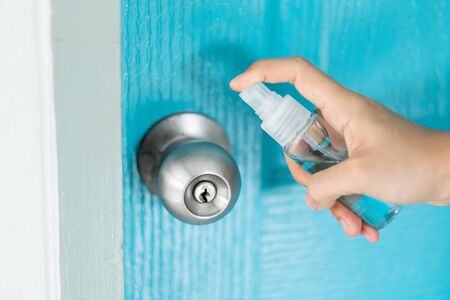 Woman hand spraying alcohol sanitizer bottle to the doorknob, against Novel coronavirus or Corona Virus Disease (Covid-19) at public indoor. Antiseptic, Hygiene and Healthcare conceptの写真素材