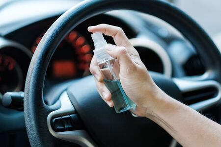 man hand spraying alcohol sanitizer on steering wheel in his car, against Novel coronavirus or Corona Virus Disease (Covid-19). Antiseptic, Hygiene and Healthcare conceptの写真素材