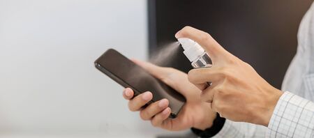 Man hand spraying alcohol sanitizer bottle to the Smartphone, against Novel coronavirus or Corona Virus Disease (Covid-19) at office or home. Antiseptic, Hygiene and Health conceptの写真素材