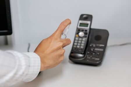 Man hand spraying alcohol sanitizer bottle to the Telephone, against Novel coronavirus or Corona...