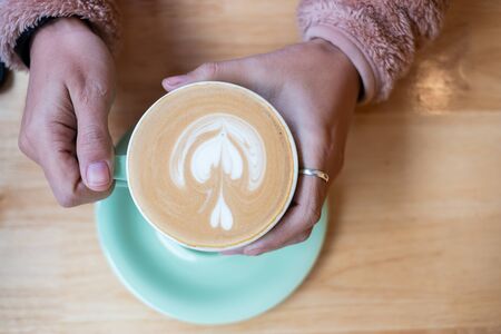 Woman holding Cup of hot art cappuccino coffee on wooden table in cafe shopの写真素材