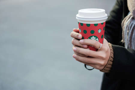 Woman hands holding hot Starbucks coffee paper cup, for Christmas and Happy New Year collection....