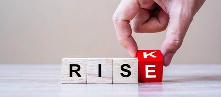 Businessman hand flipping wooden cube blocks with RISK change to RISE text on table background....