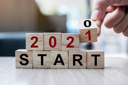 Businessman hand holding wooden cube with flip over block 2020 to 2021 START word on table background. Resolution, strategy, solution, goal, business and New Year holiday conceptsの写真素材