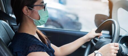 Young woman wearing protective face mask and hand controlling steering wheel in her car, against...