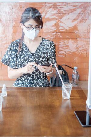 Asian woman using smartphone during dining time in restaurant with separated of shield plastic partition, protect coronavirus inflection. social distancing, new normal and life after covid-19 pandemicの写真素材