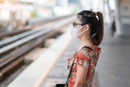 young Asian woman wearing Surgical face mask protect coronavirus inflection at public train station....