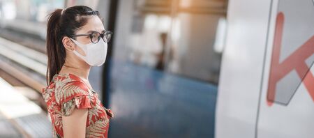 young Asian woman wearing Surgical face mask protect coronavirus inflection at public train station. social distancing, new normal and life after covid-19 pandemicの写真素材
