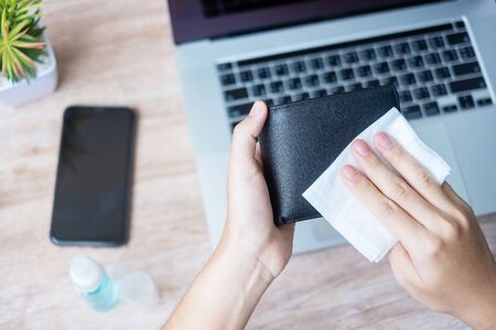 Woman cleaning money wallet and gadgets by wet wipes tissue and alcohol disinfectant on workplace during work at home, protection coronavirus (Covid-19) infection. New Normal and Clean surface conceptの写真素材