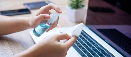 Woman cleaning laptop and smartphone by wet wipes tissue and alcohol disinfectant on workplace during work at home, protection coronavirus (Covid-19) infection. New Normal and Clean surface conceptの写真素材