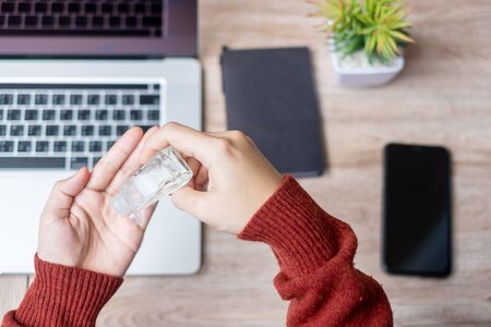 Woman cleaning hands by alcohol gel sanitizer over laptop and smartphone devices on workplace during work at home, protection coronavirus (Covid-19) infection. Personal hygiene and New Normal conceptの写真素材