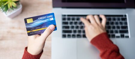 woman wearing sweater holding credit card and using laptop for online shopping while making order at...