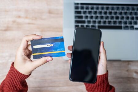 woman hand holding credit card with using smartphone and laptop for online shopping while making orders at home. business, lifestyle, technology, ecommerce, digital banking and online payment conceptの写真素材