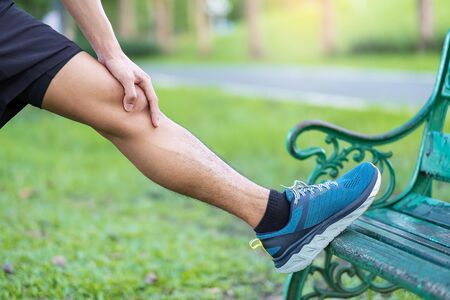 Young adult male in red sportswear stretching muscle in the park outdoor, runner man warm up ready...