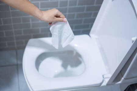 Woman hand throw paper towels in the toilet bowl. Cleaning, Lifestyle and personal hygiene conceptの写真素材
