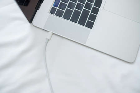 Computer laptop charging battery on bed in the bedroom at home. Technology, multiple sharing charger...
