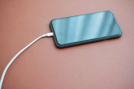 mobile smart phone charging battery on the leather sofa at home. Technology, multiple sharing and...