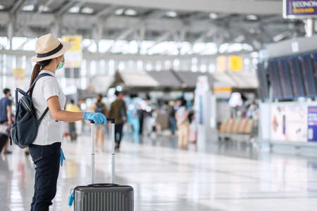Young woman traveler wearing face mask and nitrile glove holding handle luggage in airport terminal, protection Coronavirus disease (Covid-19) infection. New Normal and travel bubble conceptの写真素材