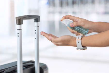 woman hand spraying alcohol sanitizer after holding handle Luggage bag in airport terminal, protection Coronavirus disease infection. New Normal, safety and travel transport under COVID-19 conceptsの写真素材