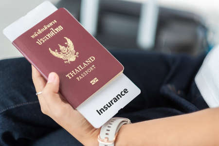Woman Hand holding Thailand passport and travel insurance document paper with luggage bag...