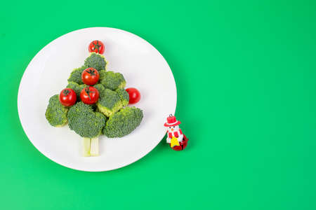 Christmas tree of organic vegetables on white plate; Broccolis and tomatoes with fork and knife on green background. Merry Xmas and happy New Year party, New You, Healthy food and vegetarian conceptの写真素材