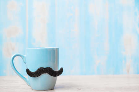 Blue coffee cups with Black mustache on wood table background in the morning. Father day and...