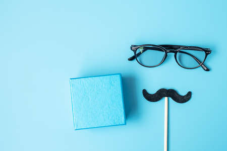 Minimal black mustache, gift and eyeglasses on blue background. Happy Father's Day and International...