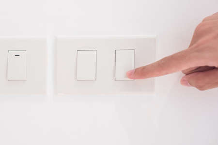 Closeup Male finger is turn on or off on light switch on white wall at home. Energy Saving, power,...