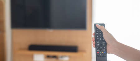 hand using remote controller for adjust Smart TV inside the modern room at home or luxury hotel