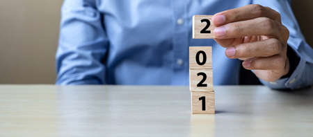 Business man hand holding wooden cube blocks with 2021 word on table background. Resolution, strategy, solution, goal, business, New Year New You and happy holiday conceptsの写真素材