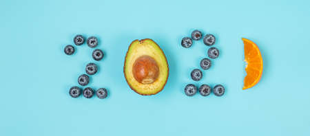 2021 Happy New Year and New You with fruits; Blueberries, Avocado and orange on blue background....