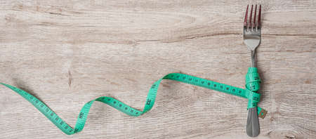 Top view Green Measuring tape wrapped around fork and knife on wooden table background. dieting, weight loss, obesity and food control conceptの写真素材