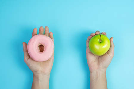 woman holding green apple and pink donut, female choose between fruit is Healthy food and sweet is...