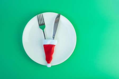 Merry Christmas with miniature Santa Claus, white plate, fork and knife on green background. Xmas, party and happy New Year conceptの写真素材